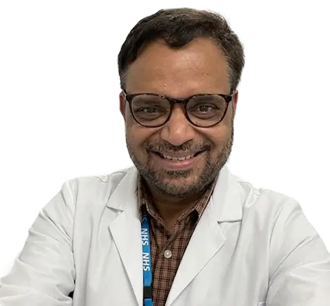 A man wearing a white lab coat and glasses, standing in a laboratory setting, focused on his work.
